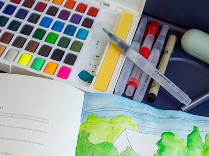 Ich packe in meinen Rucksack: Wasserpinsel, Aquarell-Malkasten, Skizzenbuch und Fineliner.